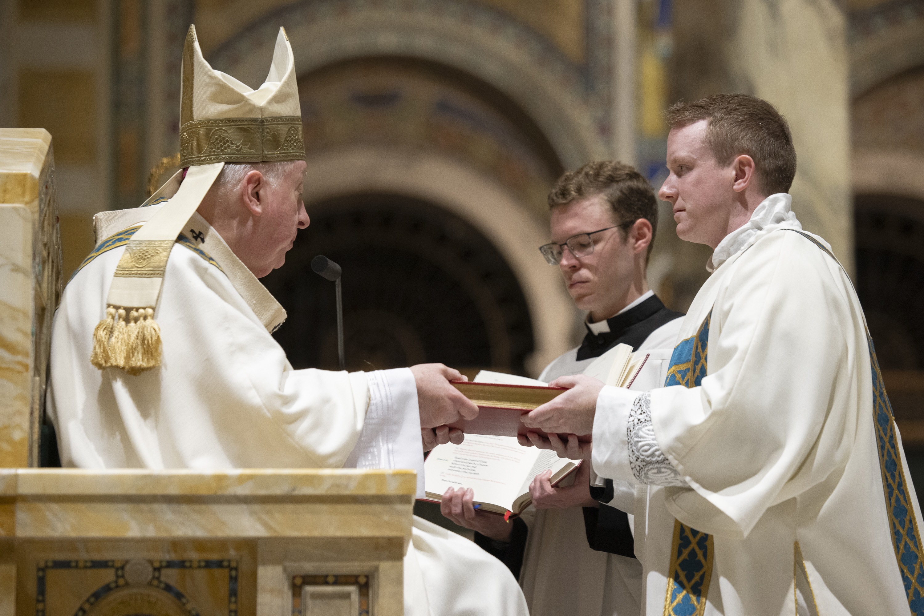 Deacon Benjamin Wolf and Archbishop Mitchell T. Rozanski hold the Book of the Gospels during the rite of ordination of deacons.